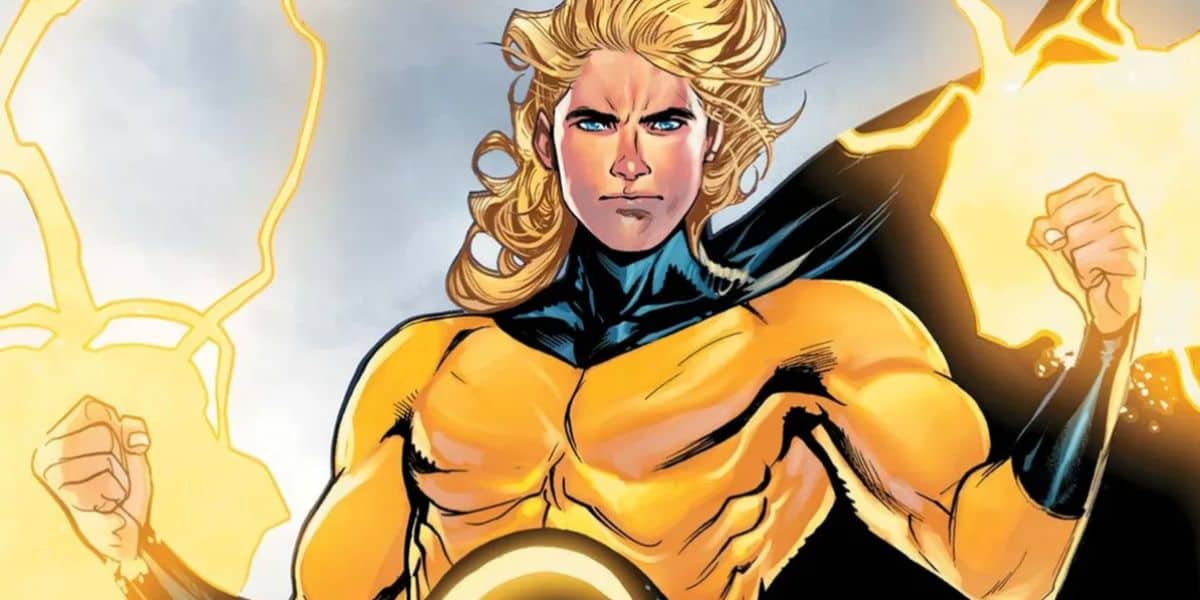 A muscular marvel superhero with long blond hair and glowing blue eyes stands confidently in a gold and black suit. Yellow energy radiates from his clenched fists, and his black cape waves behind him.