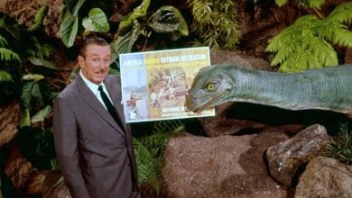 A Disney executive poses by a life-size dinosaur and vibrant attraction poster, marking 40 years of dinosaurs at Disney World.