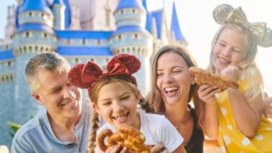 smiling family eating mickey-shaped pretzles in front of cinderella castle in magic kingdom