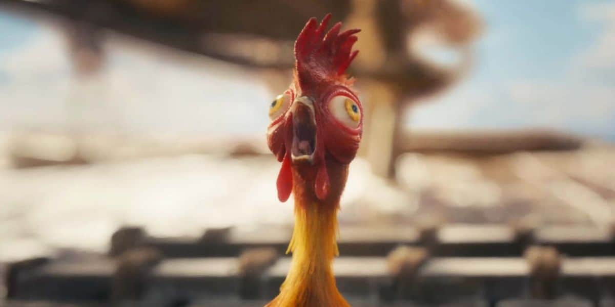 A cartoonish chicken with wide, bulging eyes and a surprised expression stands on a wooden surface, reminiscent of Hei Hei from Moana, with a blurry background.