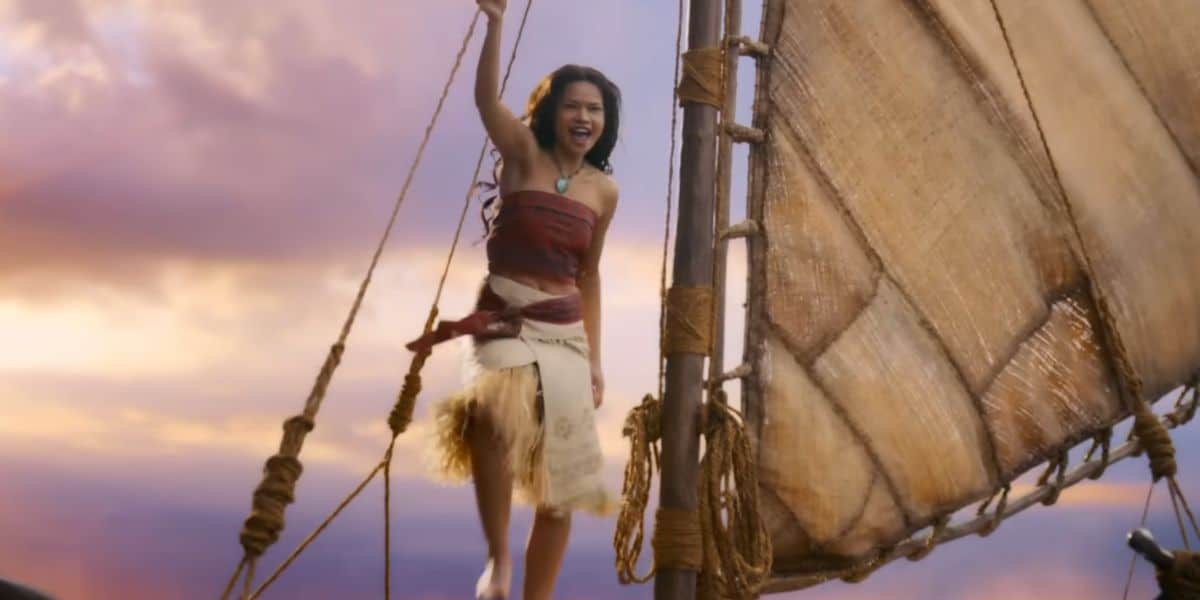 A young woman wearing a red tube top, beige skirt, and a necklace stands confidently on a sailboat, holding a rope and smiling, evoking Moana vibes against the backdrop of a vibrant sunset sky.