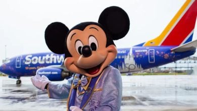 Mickey Mouse poses in front of a Southwest Airlines flight, decorated with Walt Disney World Resort 50th anniversary logos.