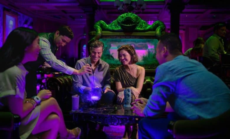 Guests gather around a table in an immersive lounge, chatting under vibrant purple and green park-inspired lighting.