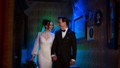 Newlyweds holding hands and beaming at each other in a nostalgic, gallery-lined hallway of Disney’s Grand Floridian Resort.