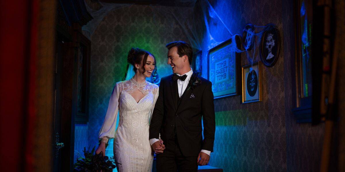 Newlyweds holding hands and beaming at each other in a nostalgic, gallery-lined hallway of Disney’s Grand Floridian Resort.