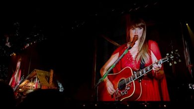 Taylor Swift plays guitar onstage in a red dress