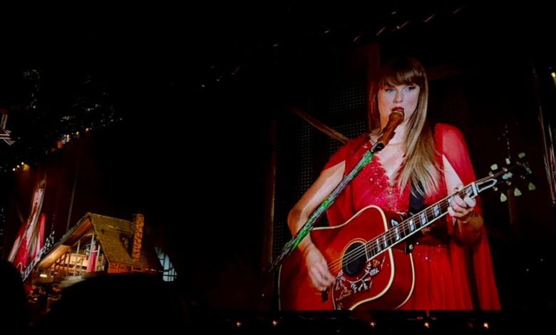 Taylor Swift plays guitar onstage in a red dress