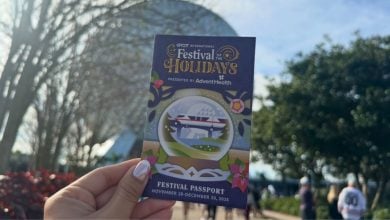 An EPCOT International Festival of the Holidays passport held up against Spaceship Earth at Walt Disney World.