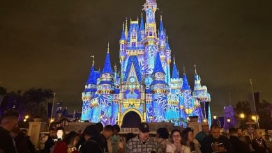 Guests gather in front of Cinderella Castle at Magic Kingdom, glowing with vibrant blue and yellow nighttime projections.