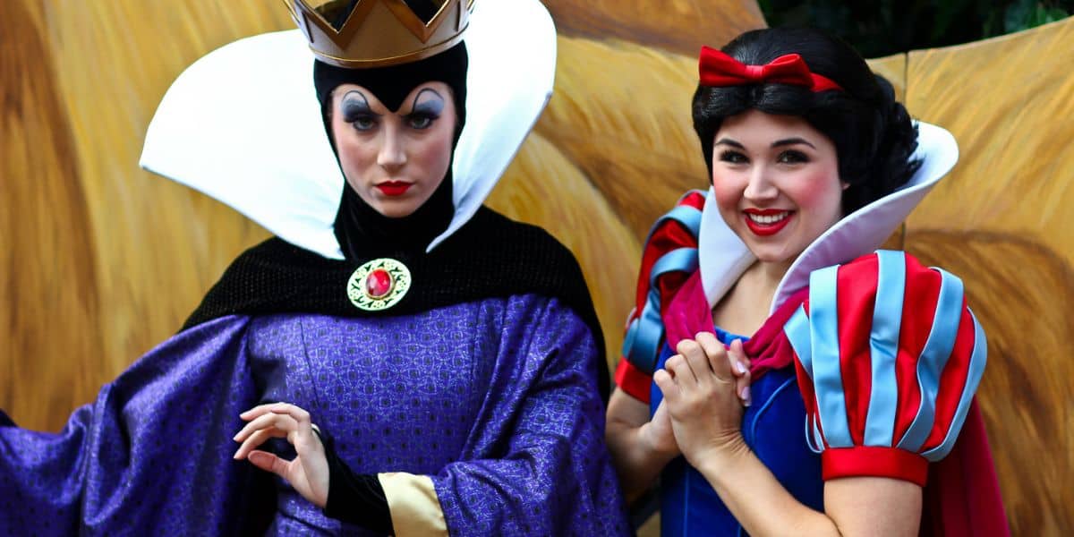 The Evil Queen and Snow White greet guests in vibrant costumes at a lively Disney park meet-and-greet outdoors.