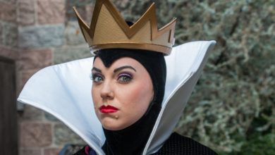 The Evil Queen from Snow White greets guests in her signature gold crown and high white collar cloak.