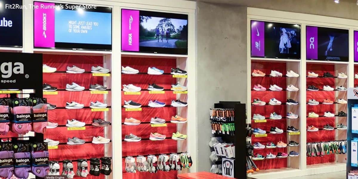 Athletic shoes and Disney-themed socks on display at Disney Springs, beneath screens featuring park news and magical ads.