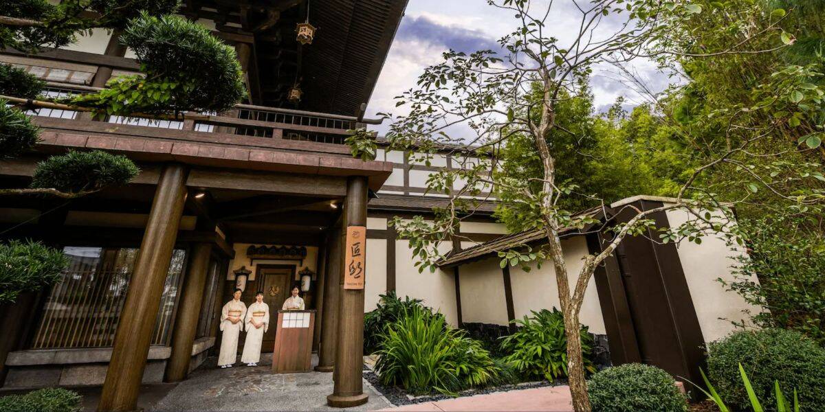Guests in traditional Japanese attire welcome visitors at the entrance of EPCOT's Japan Pavilion, lush greenery all around.