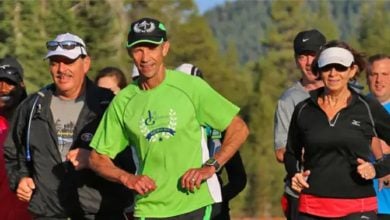 Disney fans of all ages jog in athletic gear beneath sunlit trees, channeling runDisney excitement in a magical outdoor setting.