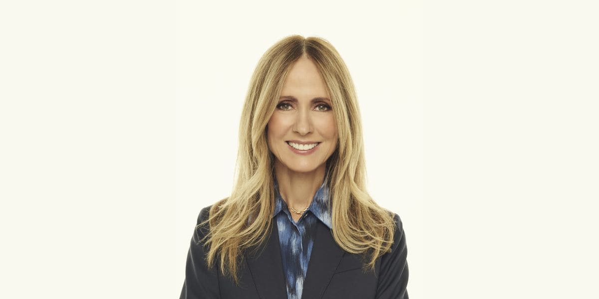 A Disney executive with long blonde hair smiles confidently, dressed smartly—embodying innovation for fans visiting the parks.