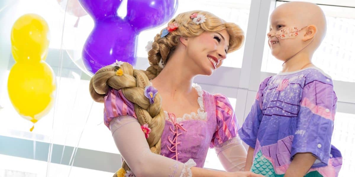 Rapunzel chats with a young child in face paint, surrounded by balloons at Orlando Hospital.