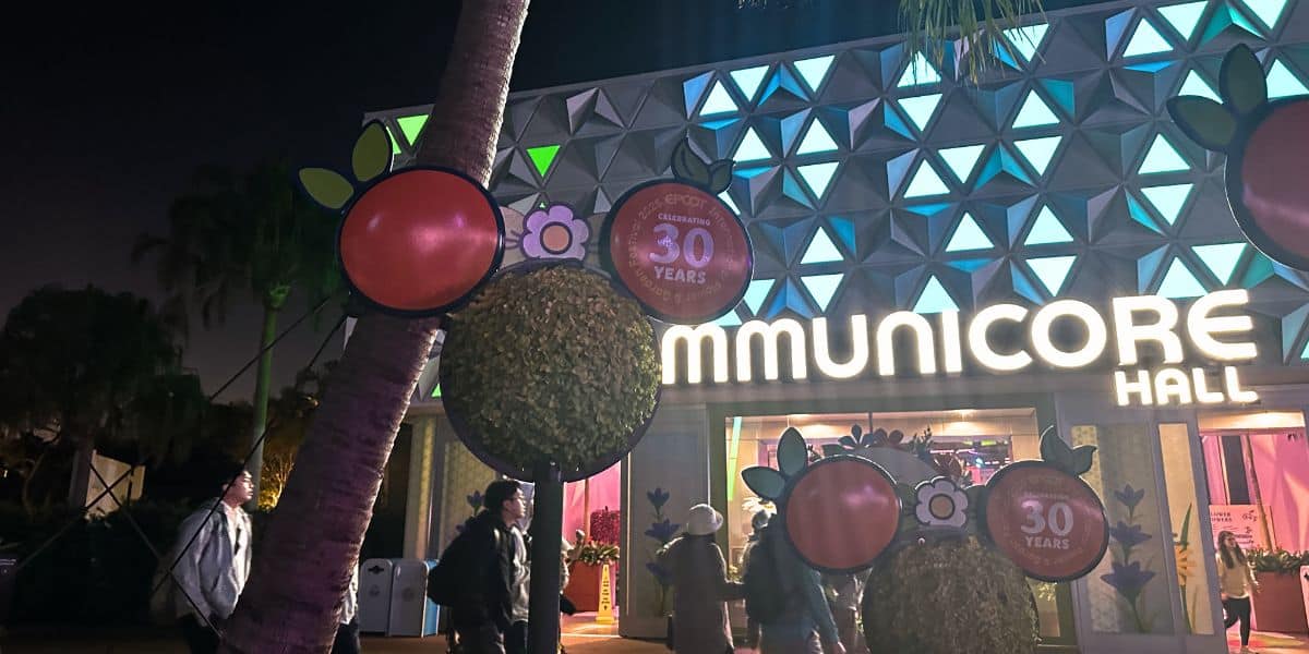 EPCOT’s CommuniCore Hall shines at night with bold orange signs celebrating its 30th anniversary during the Flower Festival.