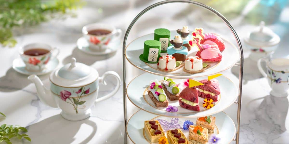 A whimsical high tea display with vibrant pastries and sandwiches, paired with teacups and a themed teapot at Disneyland.