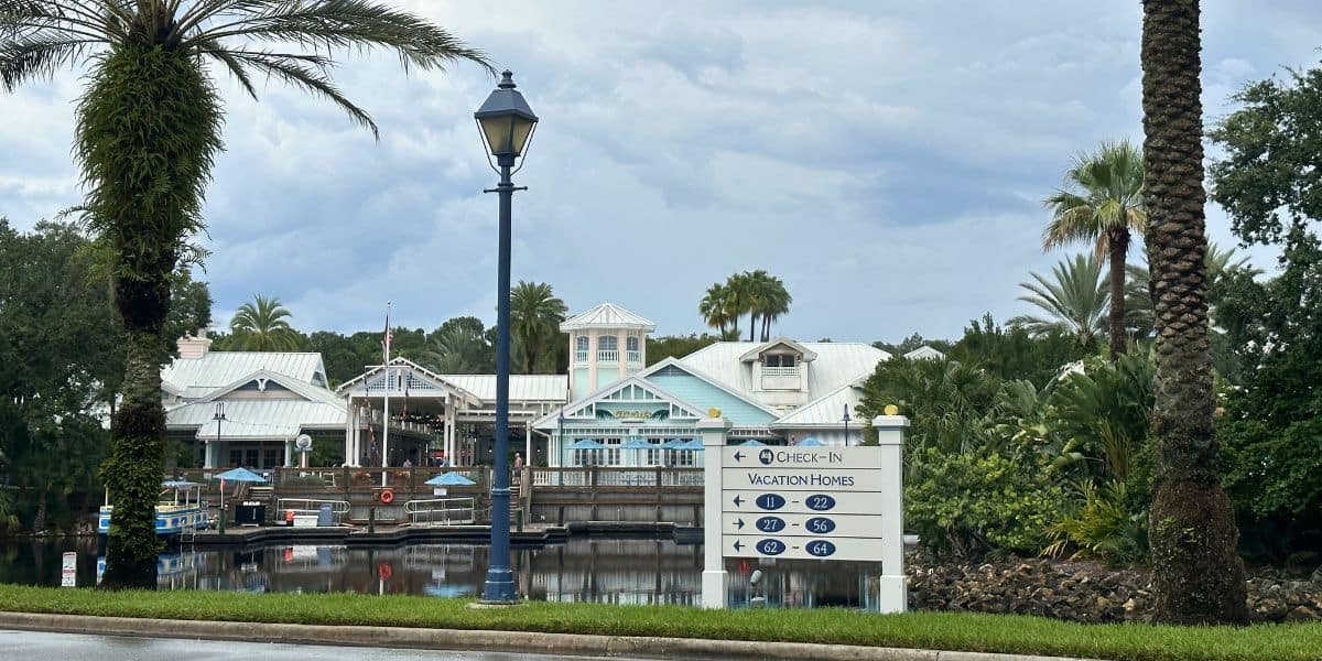 A lively resort with palm trees, a shimmering lake, and signs guiding guests to vacation villas and the grand check-in pavilion. Disney Old Key West boat service