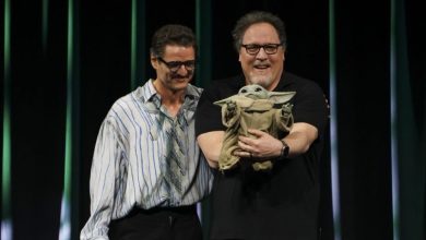 Pedro Pascal with Jon Favreau holding Grogu onstage