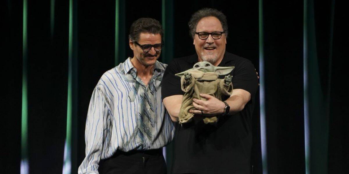 Pedro Pascal with Jon Favreau holding Grogu onstage