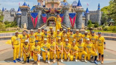 A baseball team in yellow uniforms gathers for a group photo in front of Cinderella Castle, sharing smiles and Disney magic.