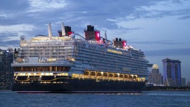 The Disney Cruise Line ship glides past Singapore’s skyline at dusk, its decks aglow with magical lights and festive ambiance.