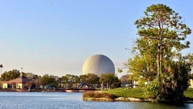 EPCOT’s iconic geodesic sphere towers over World Showcase Lagoon, surrounded by lush trees and park buildings, under a clear sky. EPCOT Food & Wine Festival 2026