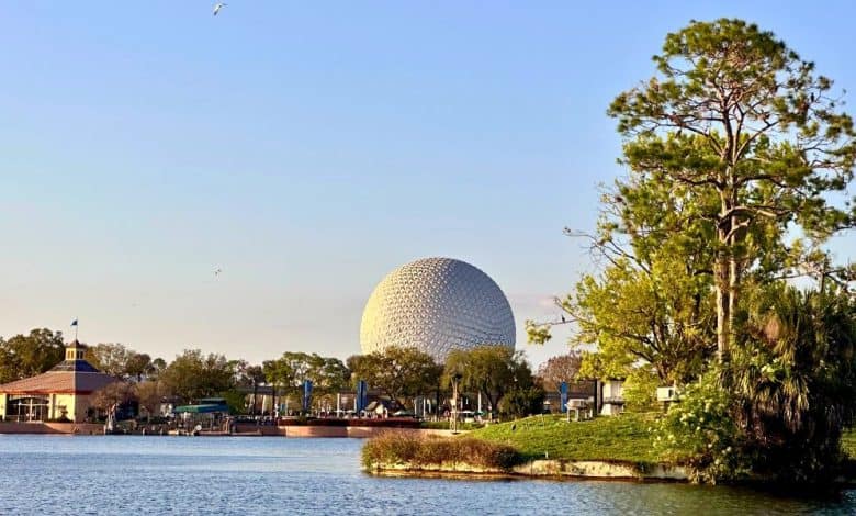 EPCOT’s iconic geodesic sphere towers over World Showcase Lagoon, surrounded by lush trees and park buildings, under a clear sky. EPCOT Food & Wine Festival 2026