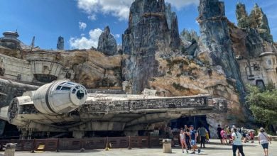 Disney World guests explore Star Wars: Galaxyโs Edge, passing the full-scale Millennium Falcon beneath towering Batuu spires.