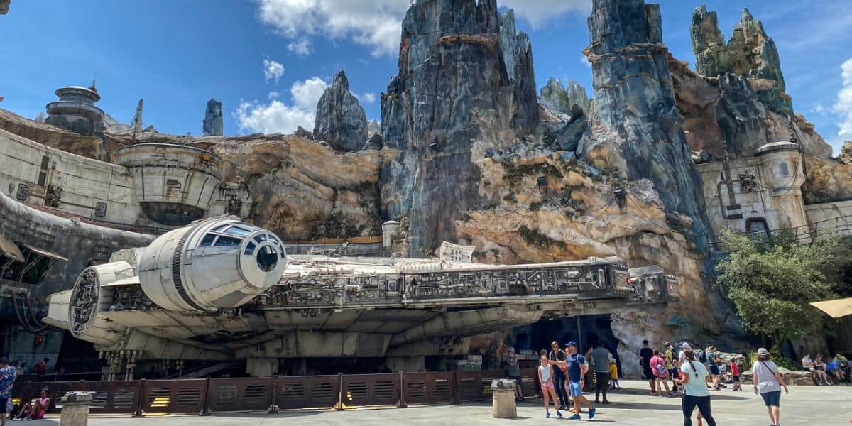 Disney World guests explore Star Wars: Galaxy’s Edge, passing the full-scale Millennium Falcon beneath towering Batuu spires.