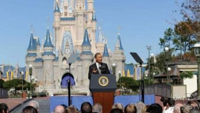 Barack Obama addresses the crowd at Cinderella Castle in Disney World as guests watch something mysteriously taken off stage.