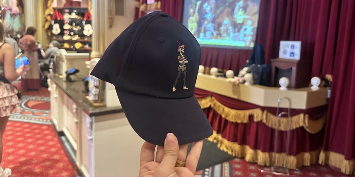 A Peter Pan cap on display at a Magic Kingdom gift shop, with red curtains and whimsical Disney-themed decorations all around.