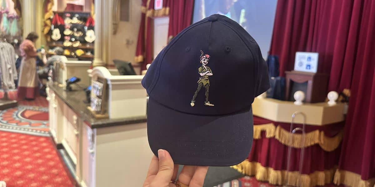 Peter Pan-themed navy cap on display among EPCOT merchandise, showcased in a store with vibrant red curtains.
