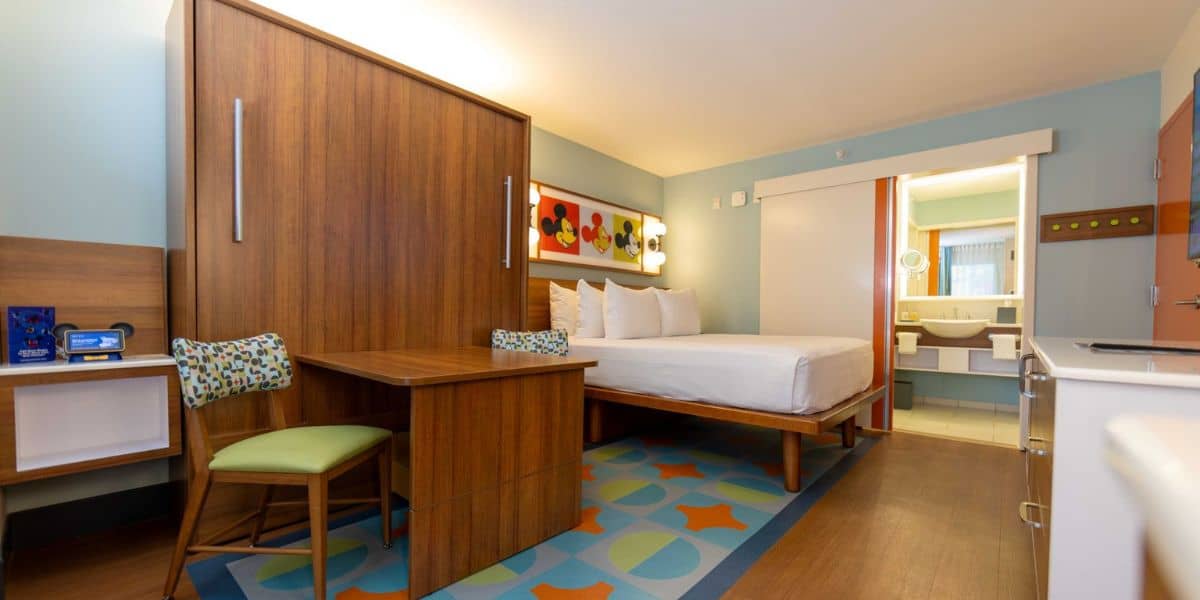 Sleek room with bed, table, chairs, and bathroom view—perfect for Disney fans wanting a comfy, budget-friendly stay near the magic.
