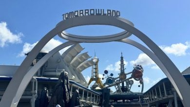 Tomorrowland’s iconic arch welcomes guests to Disney’s futuristic land, framed by sleek buildings and a brilliant blue sky.