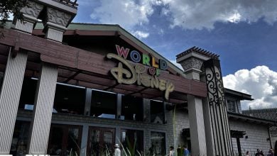 World of Disney store entrance at Disney Springs, featuring a vibrant sign against a backdrop of blue sky with fluffy clouds.