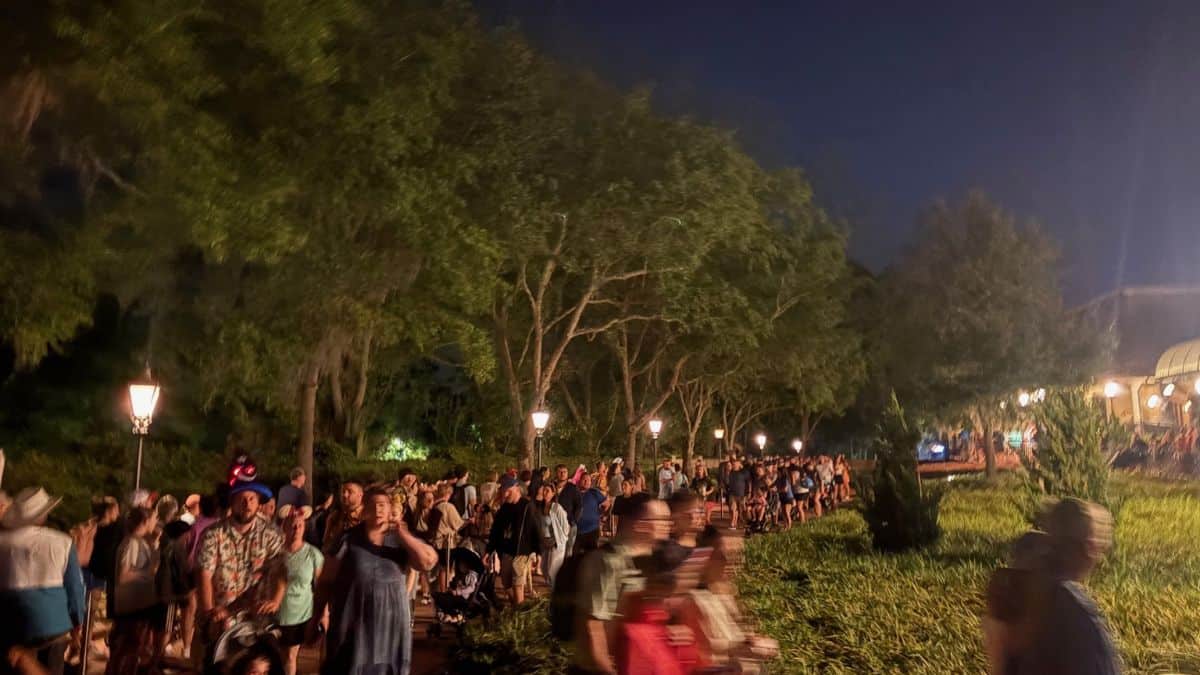Guests stream down a tree-lined walkway at night in Disney World, bathed in streetlamp glow after leaving the monorail and buses.