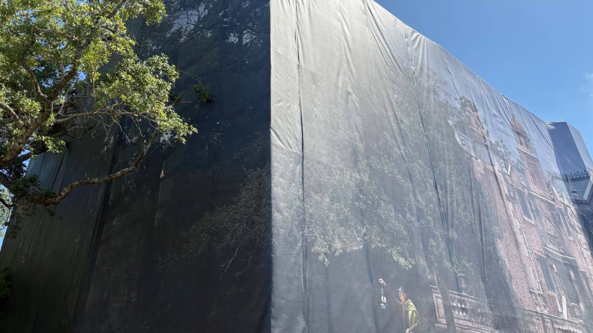 A Magic Kingdom building under a themed tarp simulates trees and bricks, teasing PeopleMover fans with its secretive transformation.