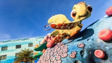 Vibrant sea turtle statue and coral decor welcome guests outside the bright blue Disney Resort, set against a sunny sky.