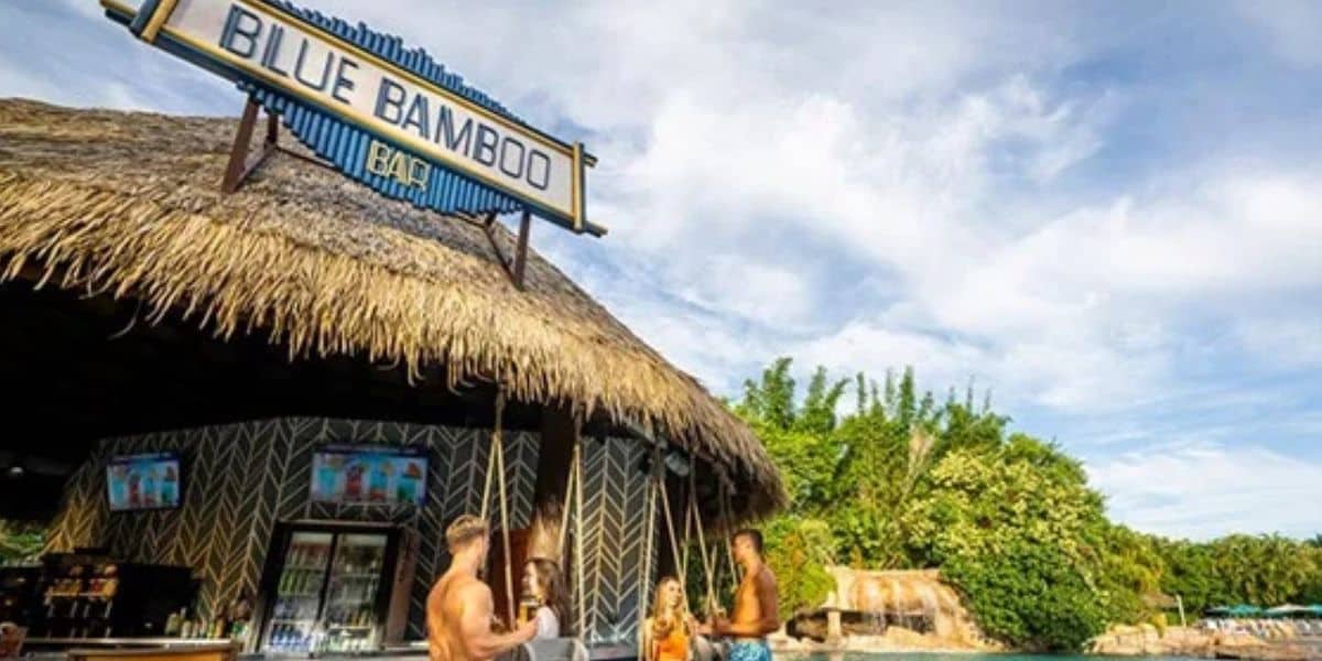 Guests mingle at the Blue Bamboo Bar, under a thatched roof and tropical foliage, capturing Discovery Cove’s Orlando summer party vibe.
