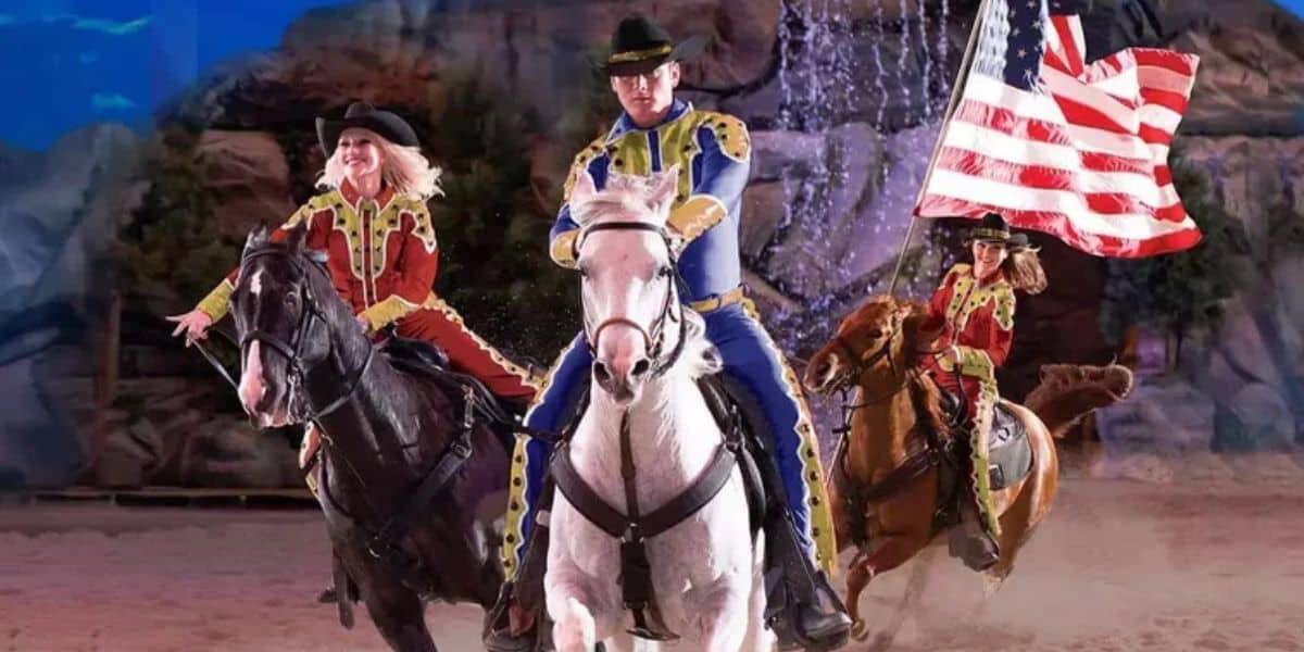 Performers in vibrant Western attire lead horseback displays, one waving the American flag, with Frontierland’s rugged scenery behind.