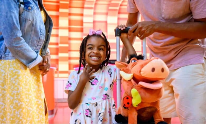 young guest with suitcase and Pumba stuffed animal waits in disney's hotel lobby with her parents