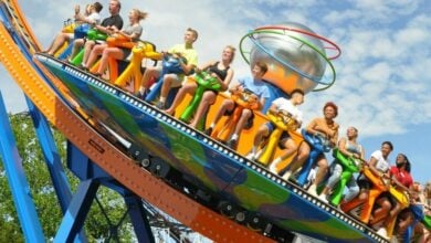 Guests laughing on the spinning Tilt-A-Whirl at Six Flags, set against a vibrant blue sky dotted with fluffy clouds.