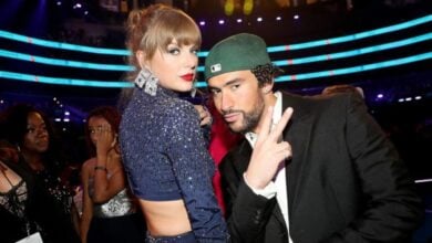 Celebrity duo dazzles at the awards, with one in a glittery blue look and the other in a green cap, spotlights shining behind them.