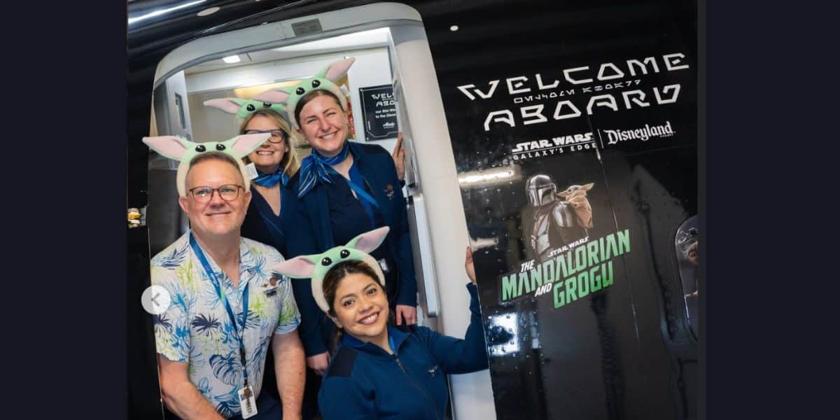 Flight attendants in Grogu ears pose by a Star Wars-themed plane decked with Disneyland magic, ready for an epic adventure.