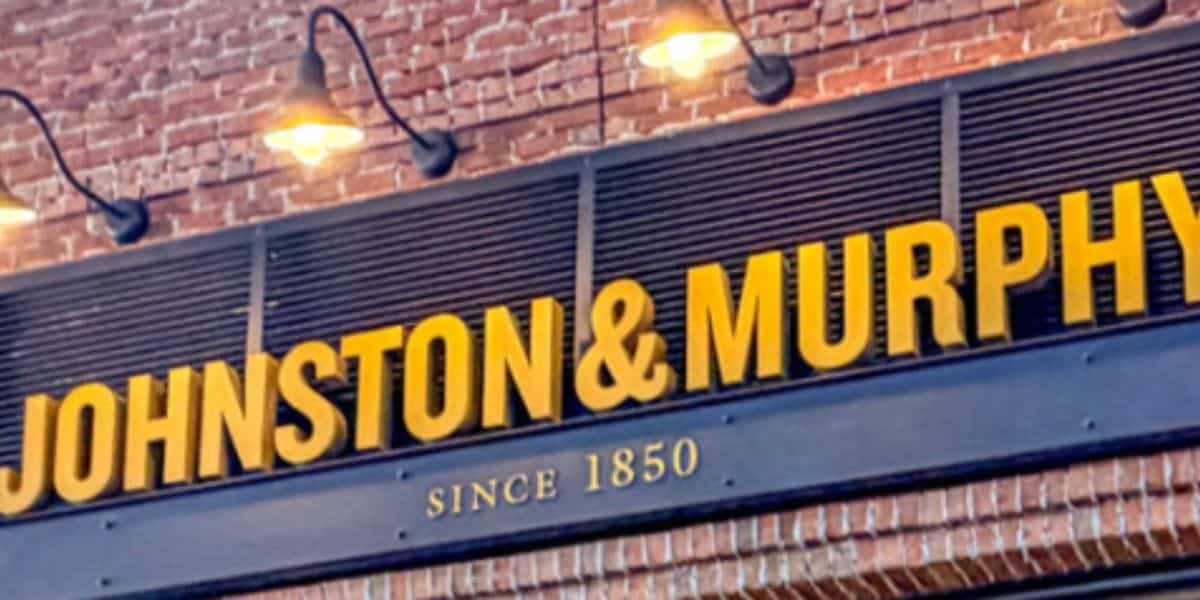 JOHNSTON & MURPHY shopfront, bright yellow sign and "Since 1850" on a classic brick wall in a lively boardwalk setting.