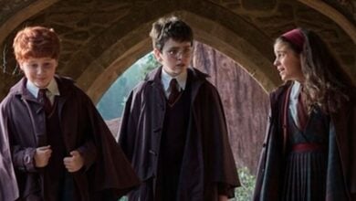 Harry, Ron, and Hermione in their Hogwarts robes chat beneath a castle archway at The Wizarding World of Harry Potter.