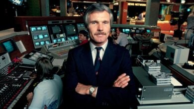 A Disney executive in a suit stands confidently in a bustling TV control room full of monitors and production gear.