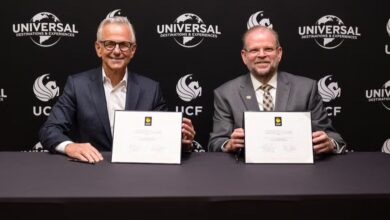 Universal and UCF executives signing documents at a table, with Universal and UCF logos displayed prominently behind them.